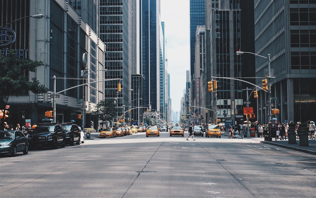 Wide city avenue with yellow taxis, parked cars, and pedestrians between tall skyscrapers